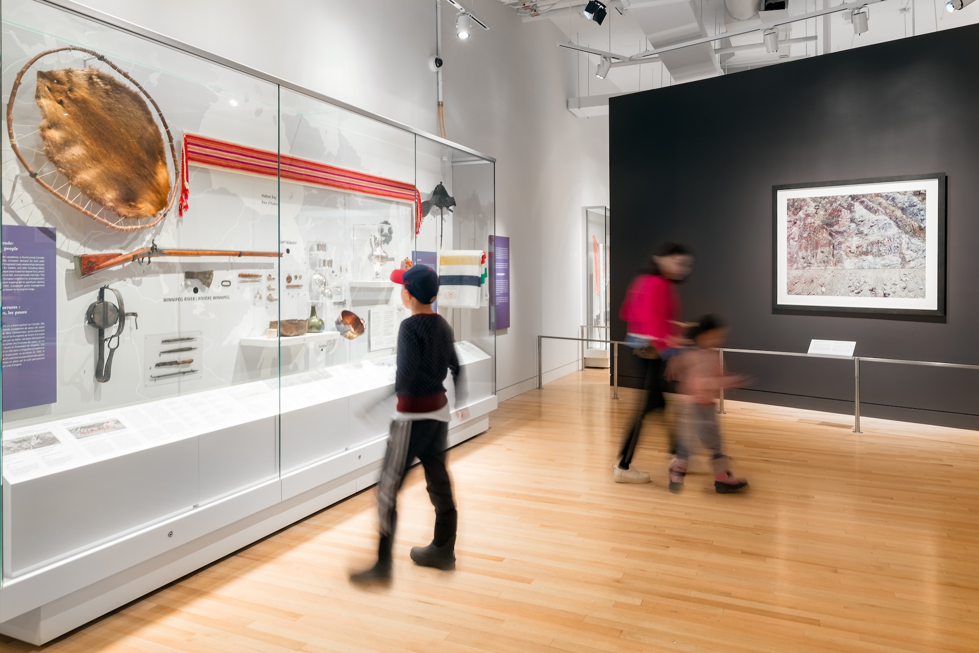 Museum gallery with glass display cases containing artifacts and two visitors walking by.