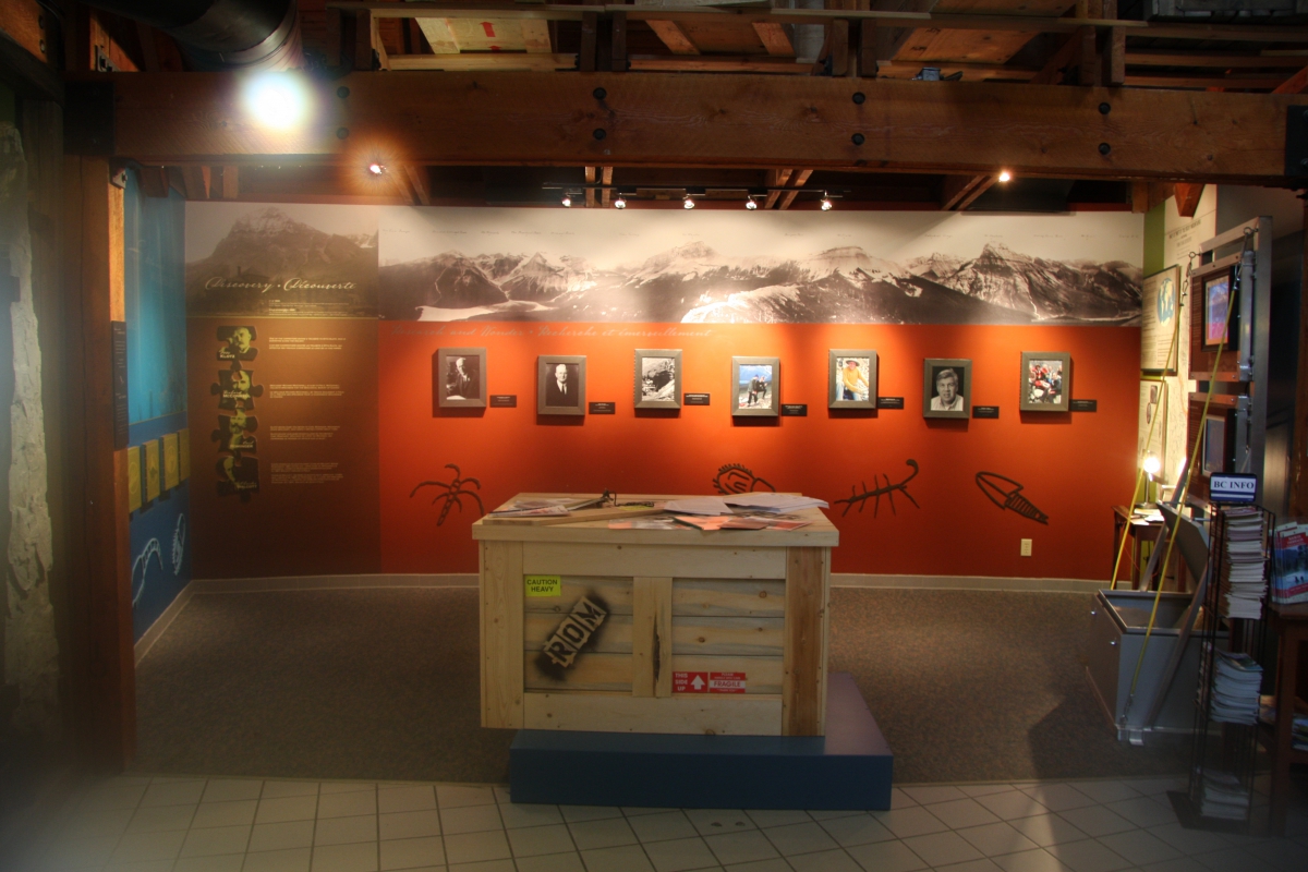 Museum exhibit space with framed black and white portraits on a red wall and a display case in the center.