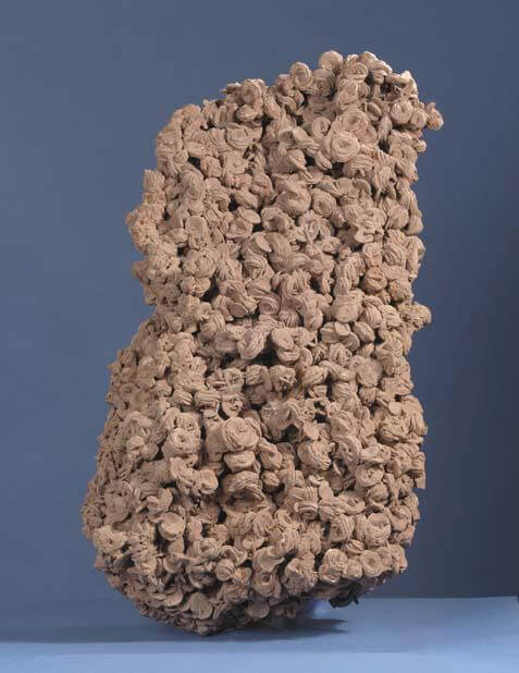 Large irregular brown termite mound with multiple small tunnels and chambers against a plain blue background.
