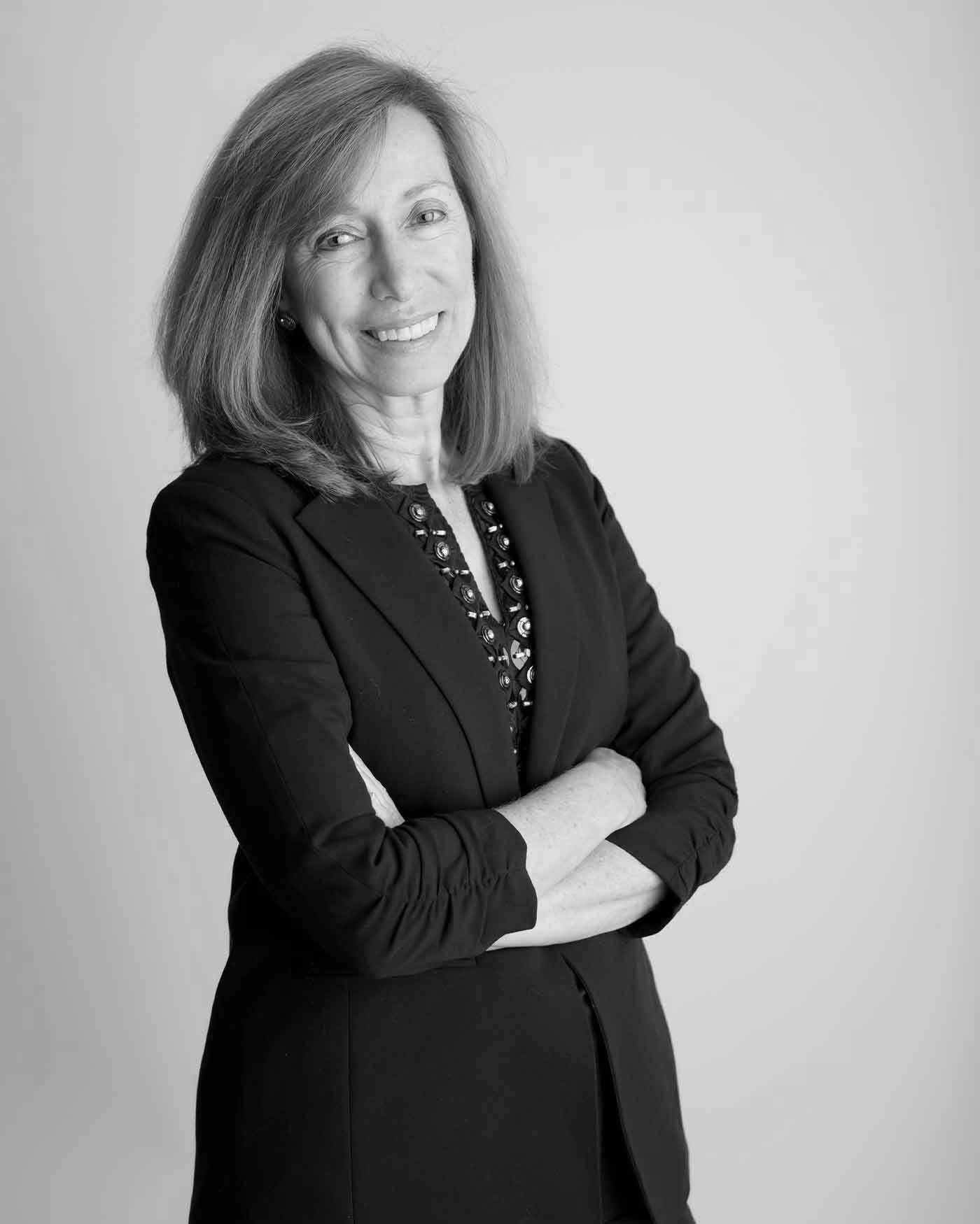 Portrait of a woman with shoulder-length hair, wearing a dark blazer and patterned blouse, smiling with arms crossed.