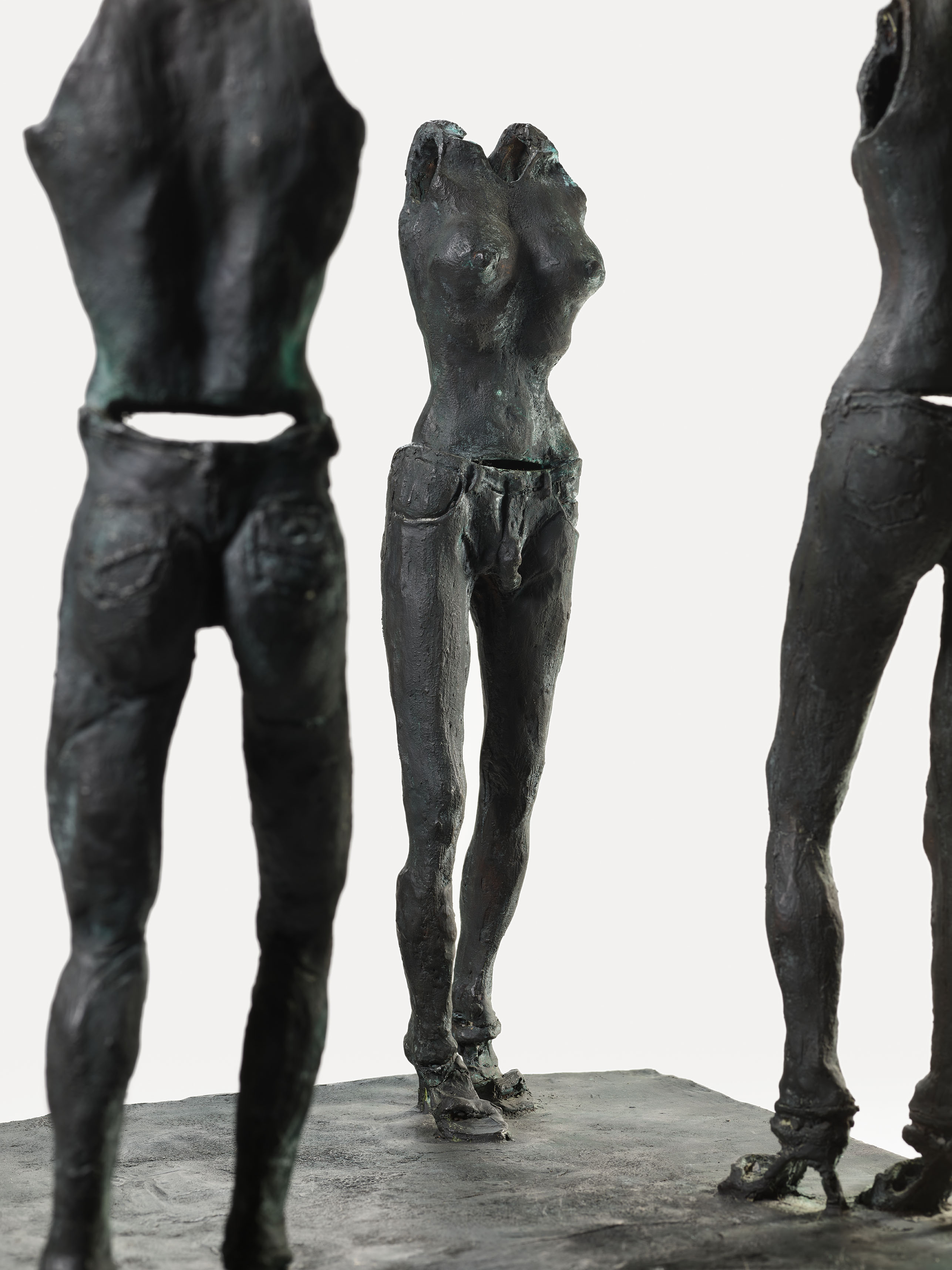 Three dark bronze abstract sculptures of human torsos standing on a flat base.