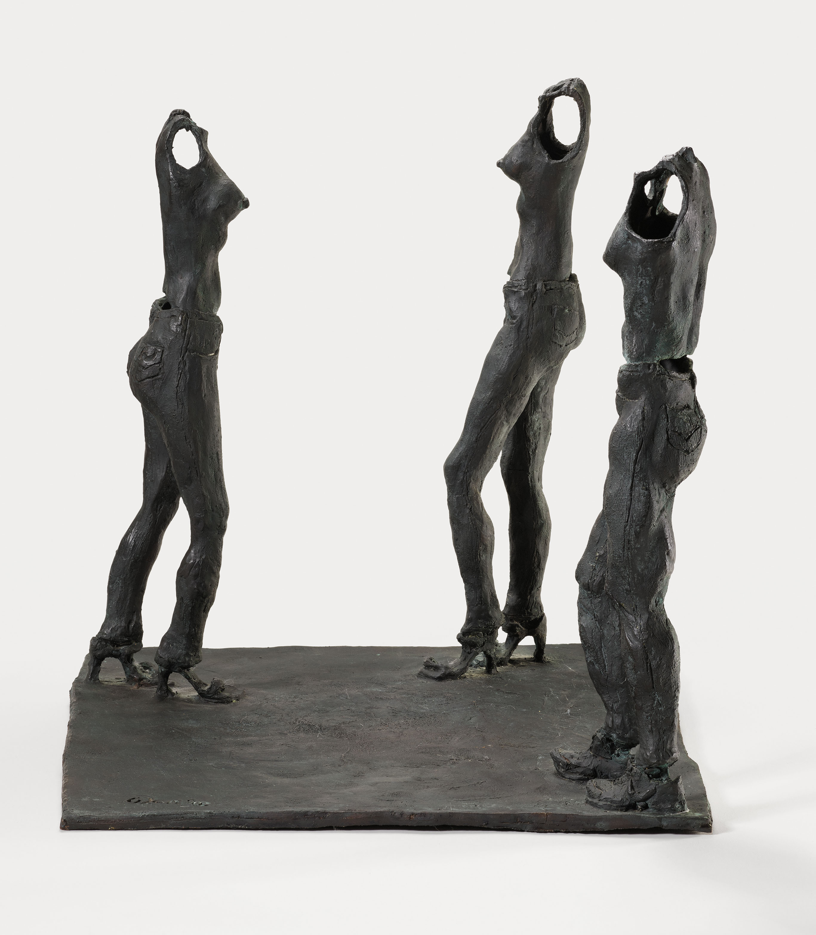 Bronze sculpture of three standing female figures with stylized, elongated forms on a flat base.