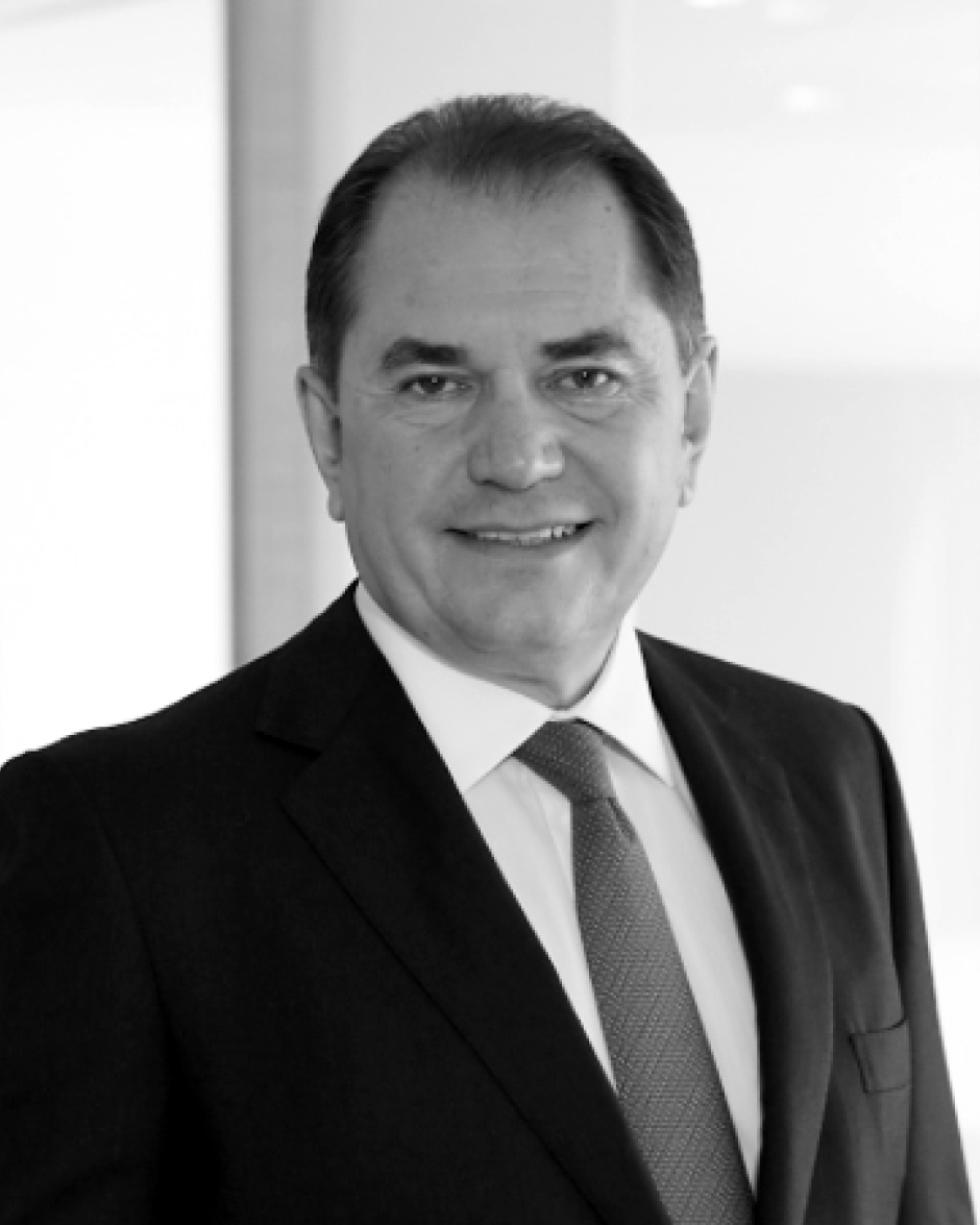 A black-and-white portrait of a man in a suit and tie, smiling, with a light background.