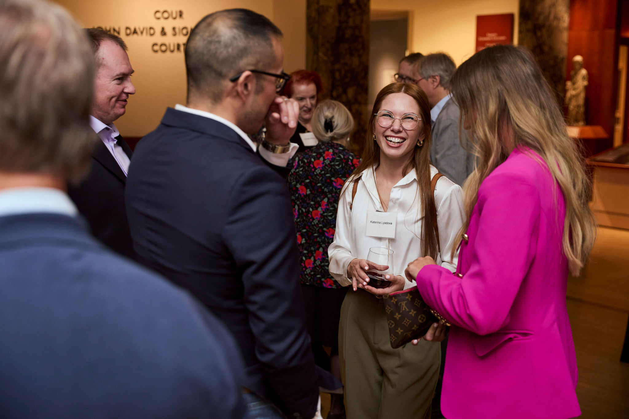 A group of adults socializing indoors, with one woman holding a wine glass and smiling.