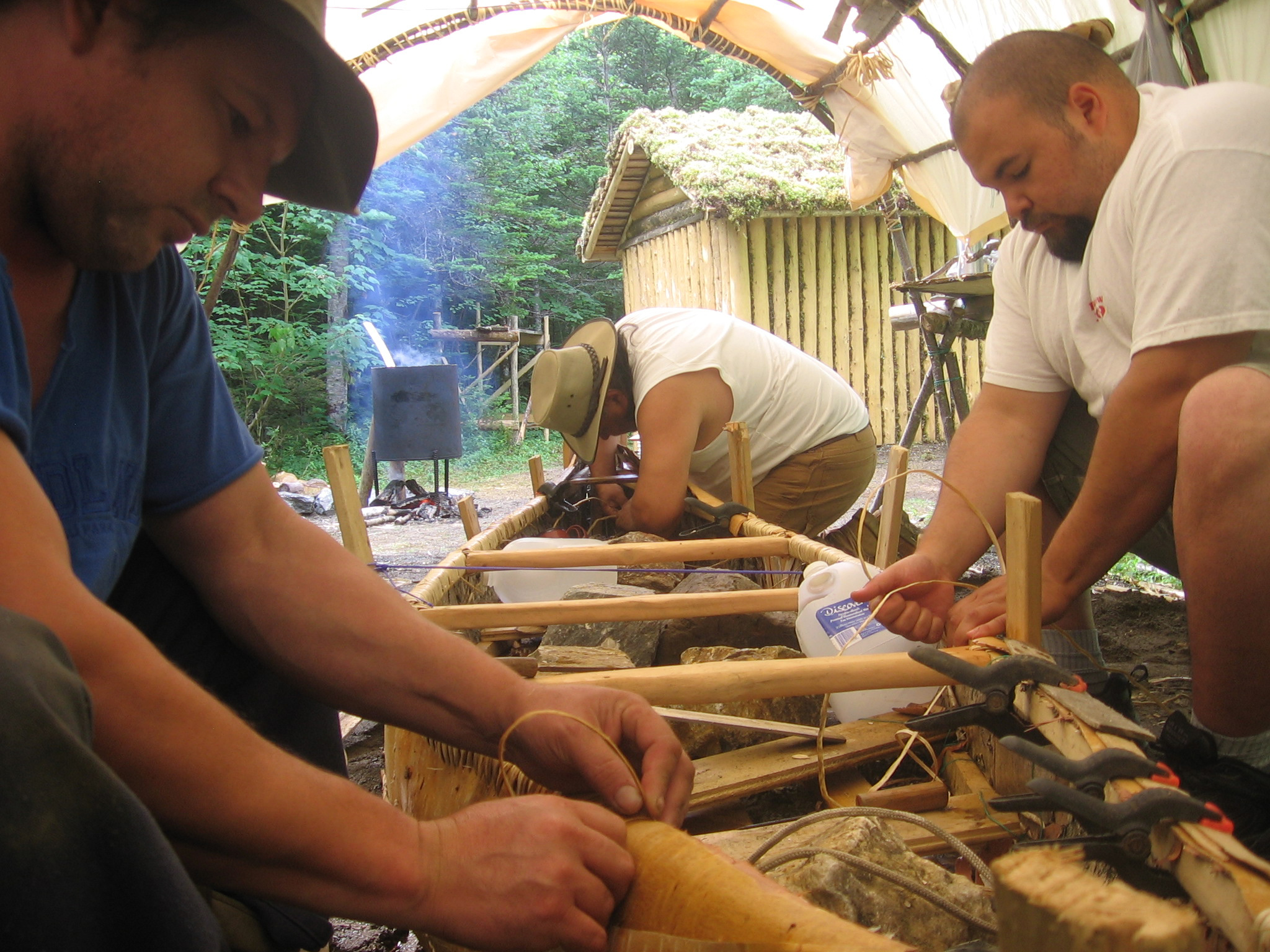 Trois hommes fabriquant un canoë en écorce de bouleau.