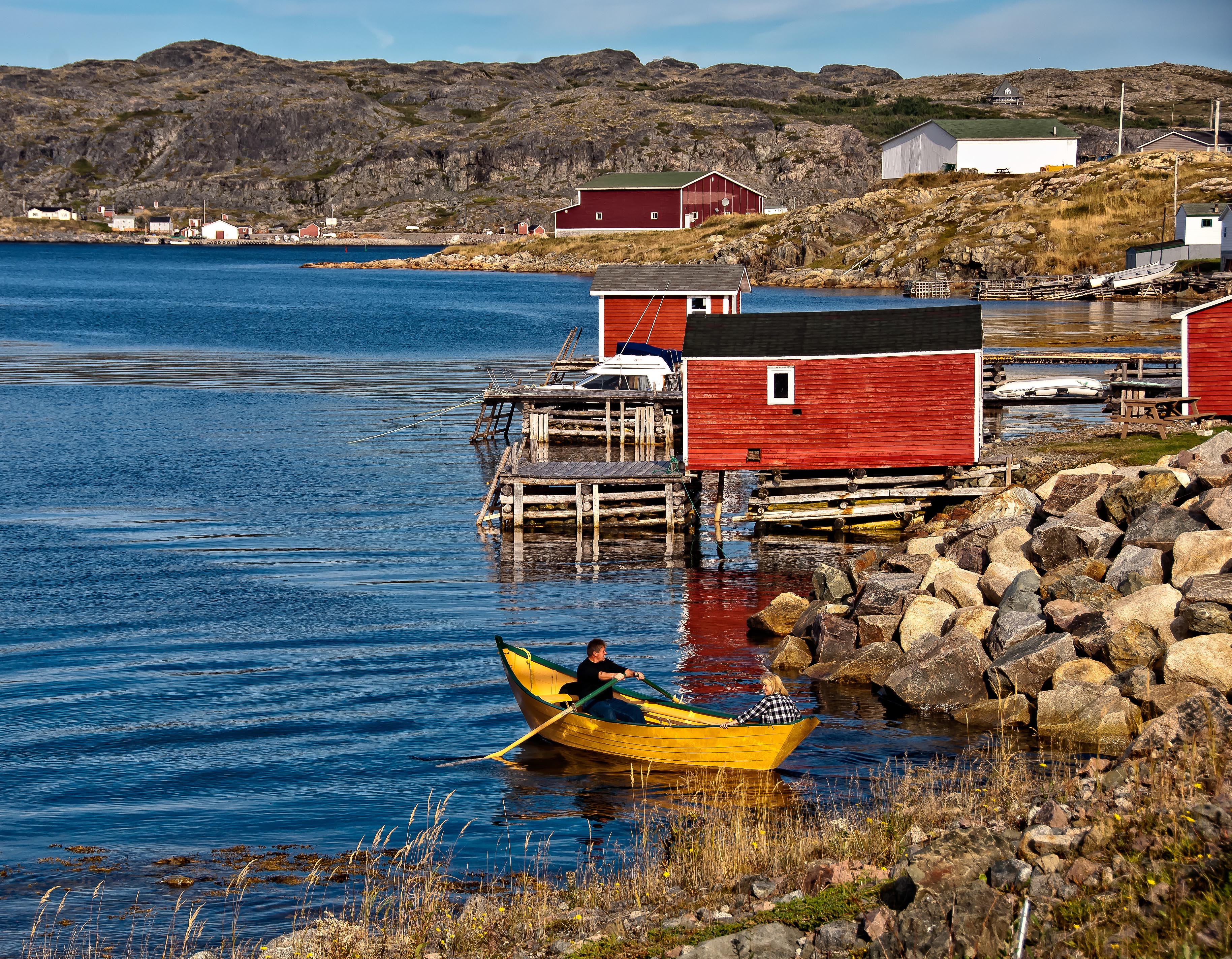Maisons colorées au bord de la mer avec une barque au premier plan.