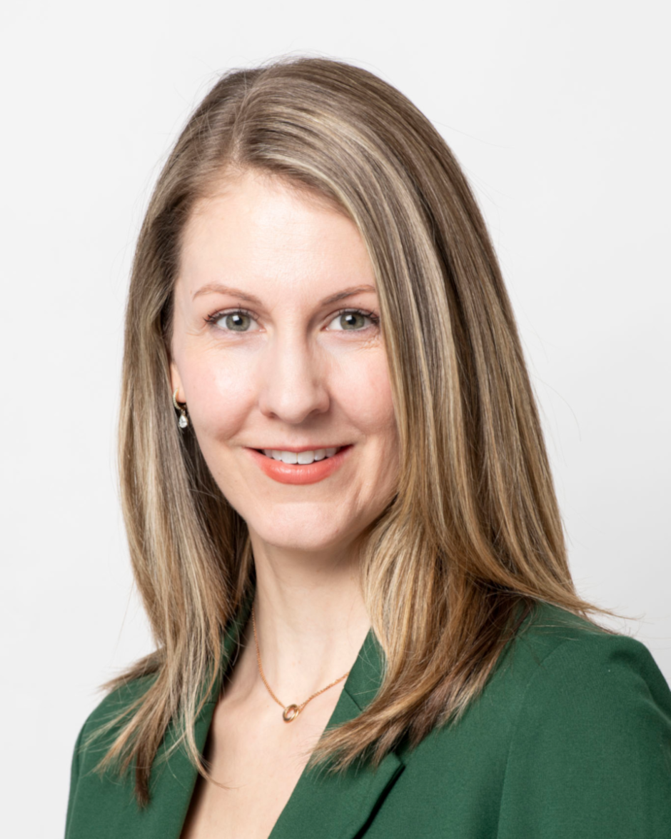Portrait of a woman with straight blonde hair wearing a green blazer and a gold necklace against a white background.