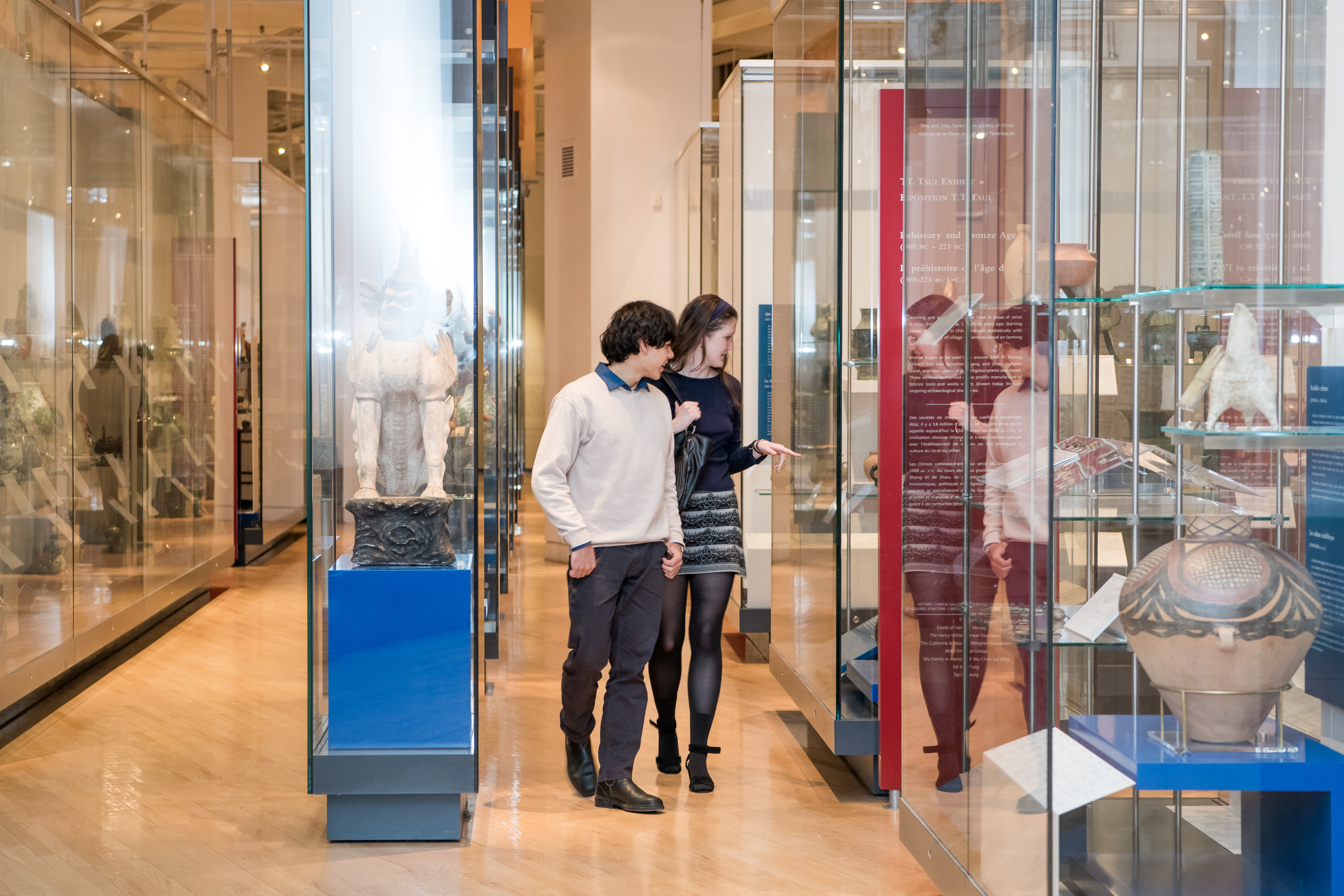 Two people wearing face masks looking at artifacts displayed in glass cases inside a museum gallery.
