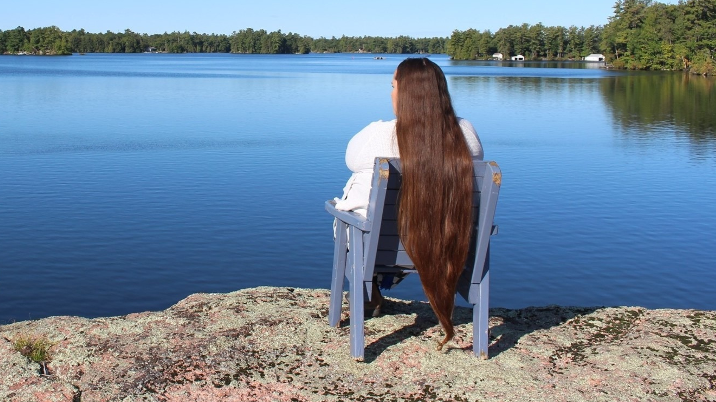 Une femme aux cheveux longs est assise sur une chaise surplombant un lac d'un bleu limpide.