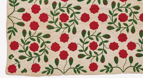 Quilt with a pattern of red flowers and green leaves on a cream background.