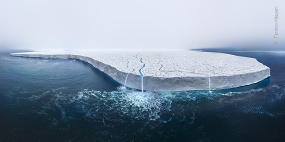 A large icy iceberg floating in dark ocean water under a clear sky.