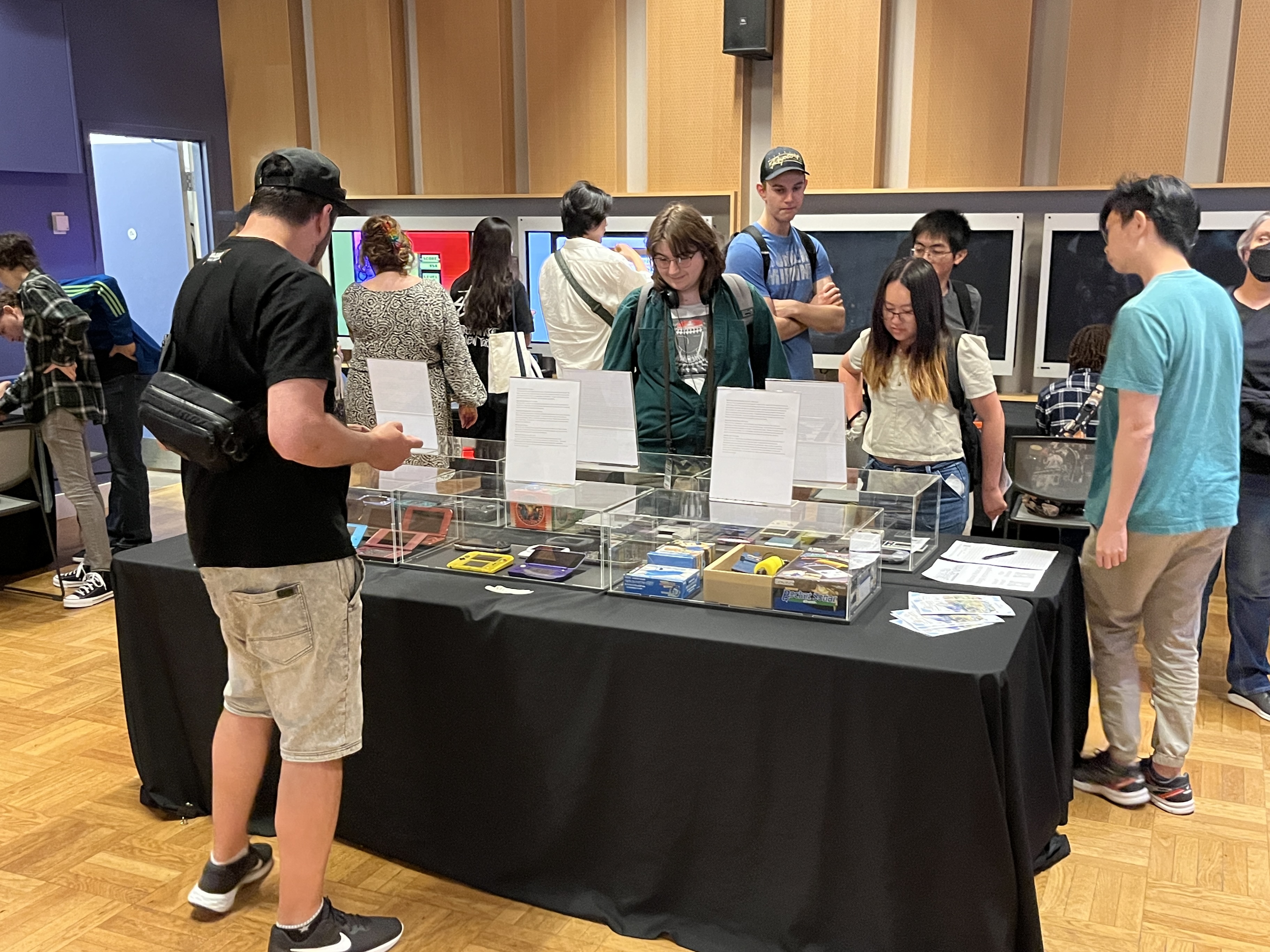 Several people viewing a table covered in a selection of gaming consoles