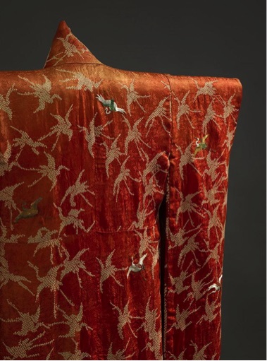 Close-up of an orange-red fabric with a shiny gold floral and leaf pattern.