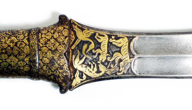 Close-up of a dagger blade with intricate gold inlay designs featuring mythical creatures and foliage.