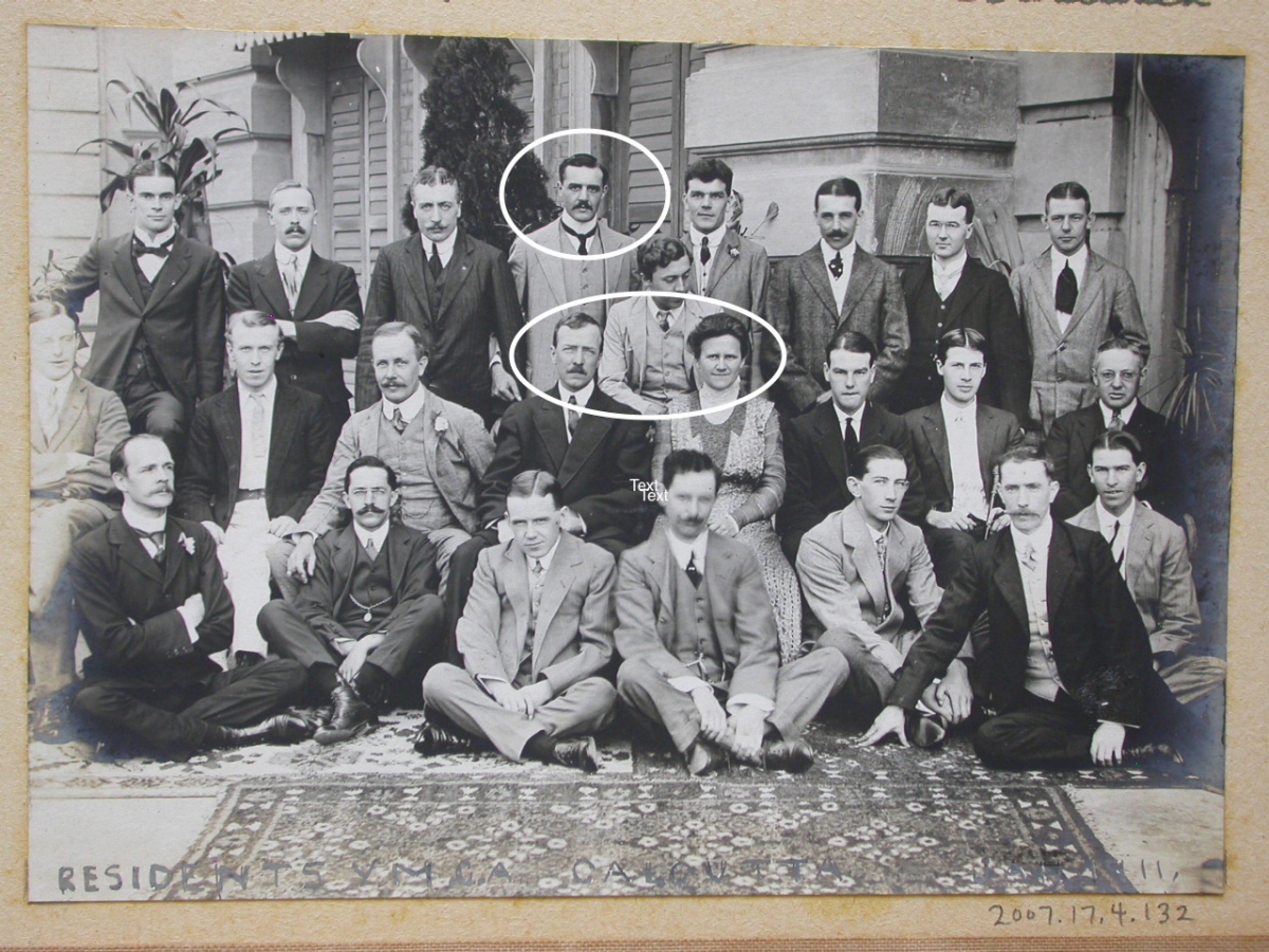 A black-and-white group photograph showing 22 men, some sitting and some standing, in front of a building.