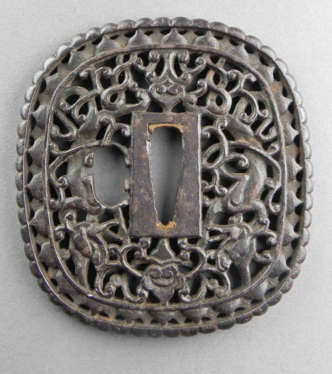 Square metal tsuba with intricate openwork floral and vine patterns surrounding a central rectangular opening.