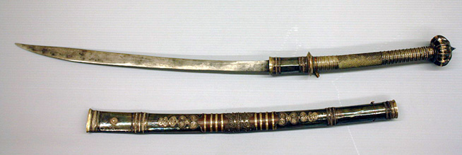 Japanese sword with a dark hilt and an ornate black and gold scabbard.