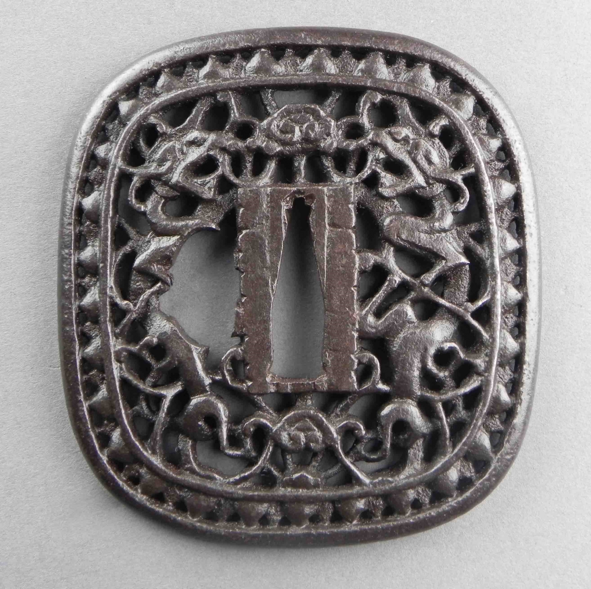 Square-shaped metal tsuba (Japanese sword guard) with intricate openwork designs.