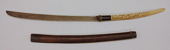 Japanese sword with a curved white handle and brown scabbard placed below it on a white surface.