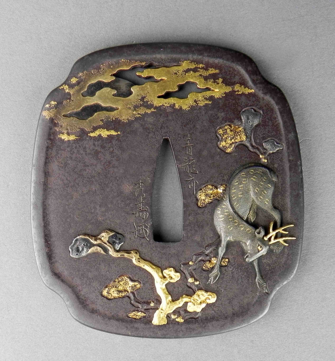 Iron tsuba with gold accents depicting a deer under a tree and clouds in a dark patina background.