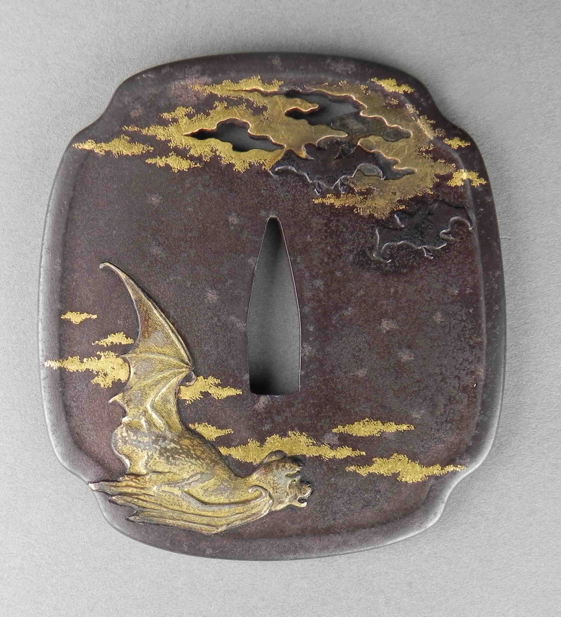 Iron tsuba sword guard with gold inlaid design of a seated figure and clouds.