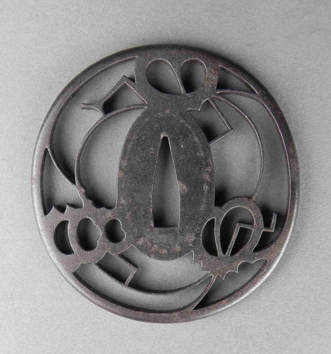 Round, dark metal tsuba with abstract cut-out shapes around the central oval opening.