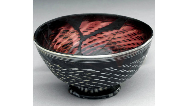 Black ceramic bowl with textured red interior and exterior decorated with horizontal white lines.