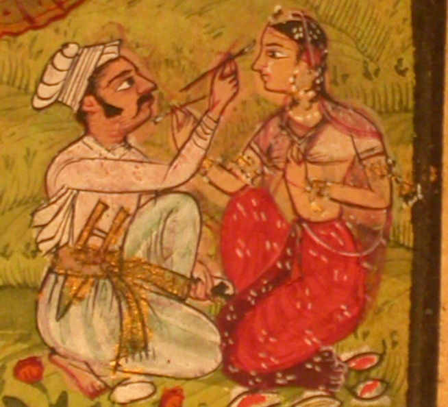 A man painting the face of a seated woman dressed in red with floral decorations on a green background.
