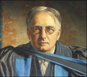 Portrait of an older man with glasses wearing a dark robe and a light blue academic stole.