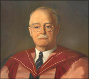 Portrait of an older man with glasses, a mustache, and a burgundy academic gown over a white shirt and tie.