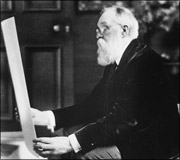 An elderly man with glasses and a beard examining a rolled-up document or blueprint.
