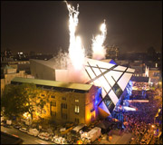 Nighttime view of the illuminated Royal Ontario Museum Michael Lee-Chin Crystal extension with fireworks overhead and a crowd below.