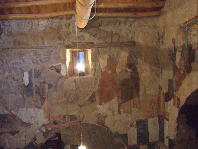 Ancient stone wall with faded fresco fragments and a small rectangular window letting in light.