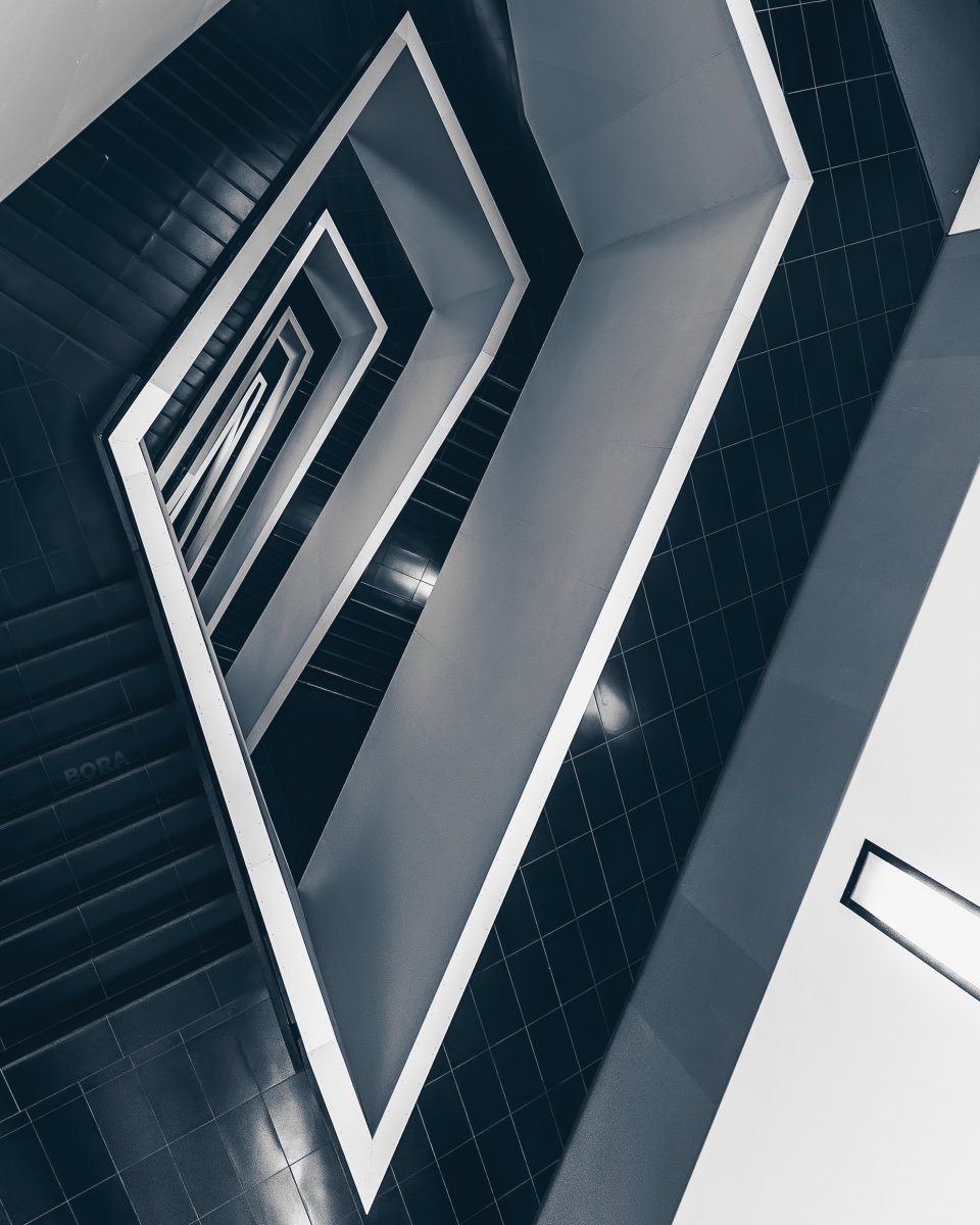 Abstract upward view of a square spiral staircase with black steps and white walls.