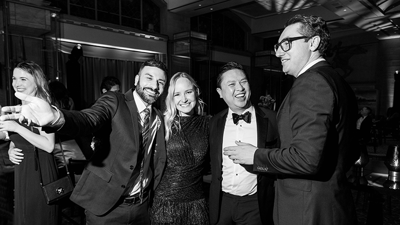 Five people in formal attire smiling and posing indoors at a social event.
