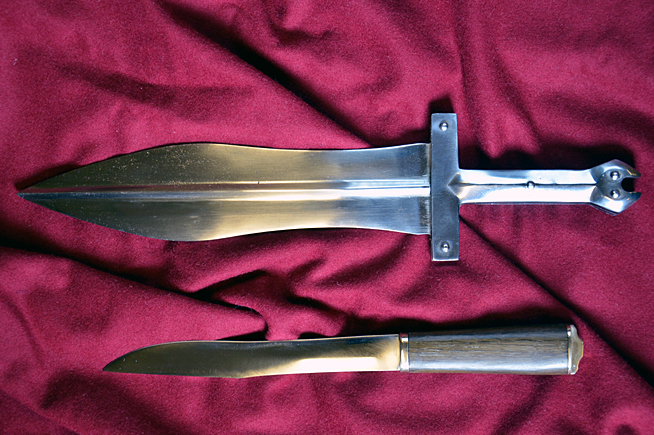 Two double-edged daggers with metal handles laid on a red fabric background.