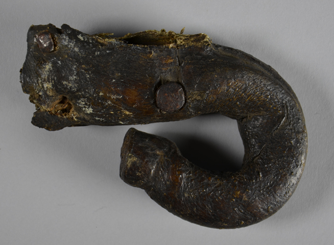 Charred and partially preserved wooden artifact shaped like a hook with a loop at one end.