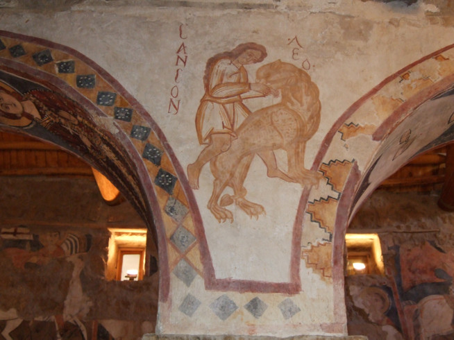 Fresco painting of a person with the text "Lamon" above on a curved wall inside a stone building.
