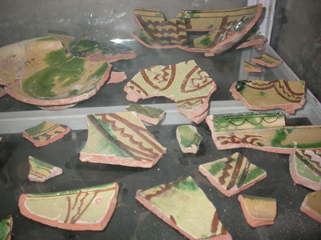 Fragments of pottery decorated with green and dark red geometric and linear patterns on a black surface.