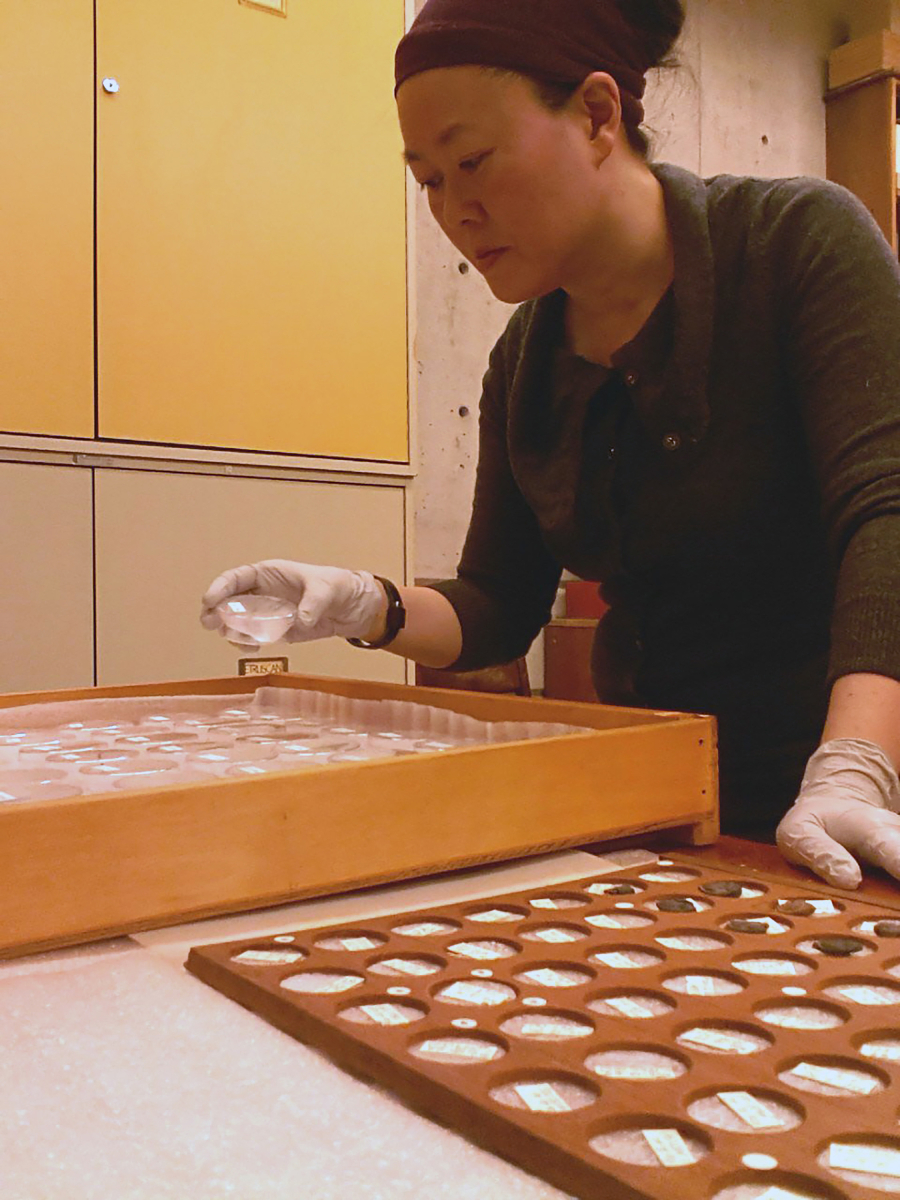 A person wearing white gloves is working with a wooden tray containing oval-shaped seals on a table.