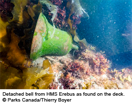 Detached bell from HMS Erebus covered in marine growth underwater on the deck.
