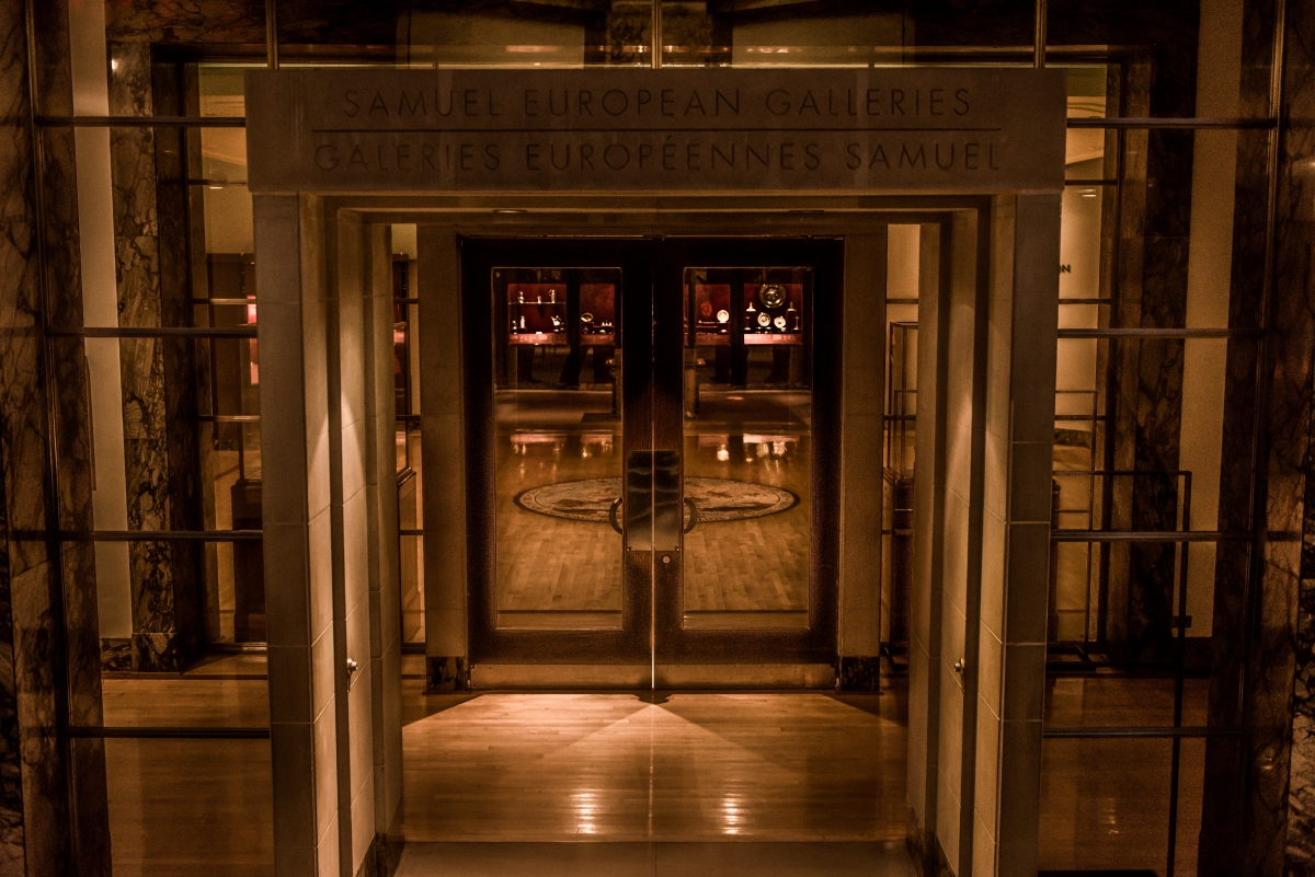 Entrance with glass doors reflecting interior lighting and the text Above the door reads: "CANADA'S EUROPEAN GALLERIES ROYAL ONTARIO MUSEUM" in dark letters on a stone frame.