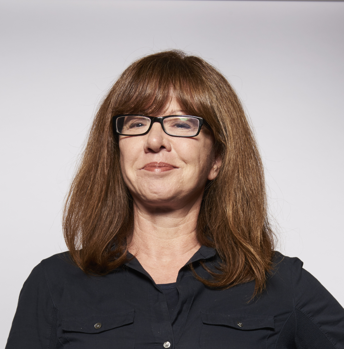 A woman with straight brown hair and glasses wearing a black button-up shirt against a plain light background.