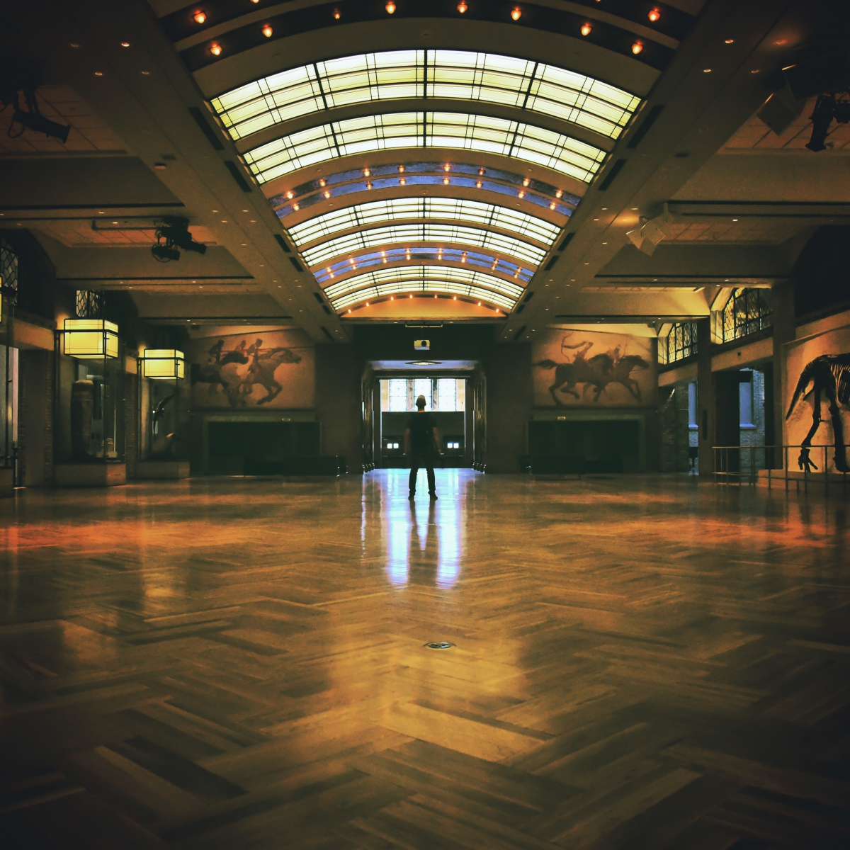 Interior view of a large museum hall with a decorative arched skylight ceiling and polished wooden floor.