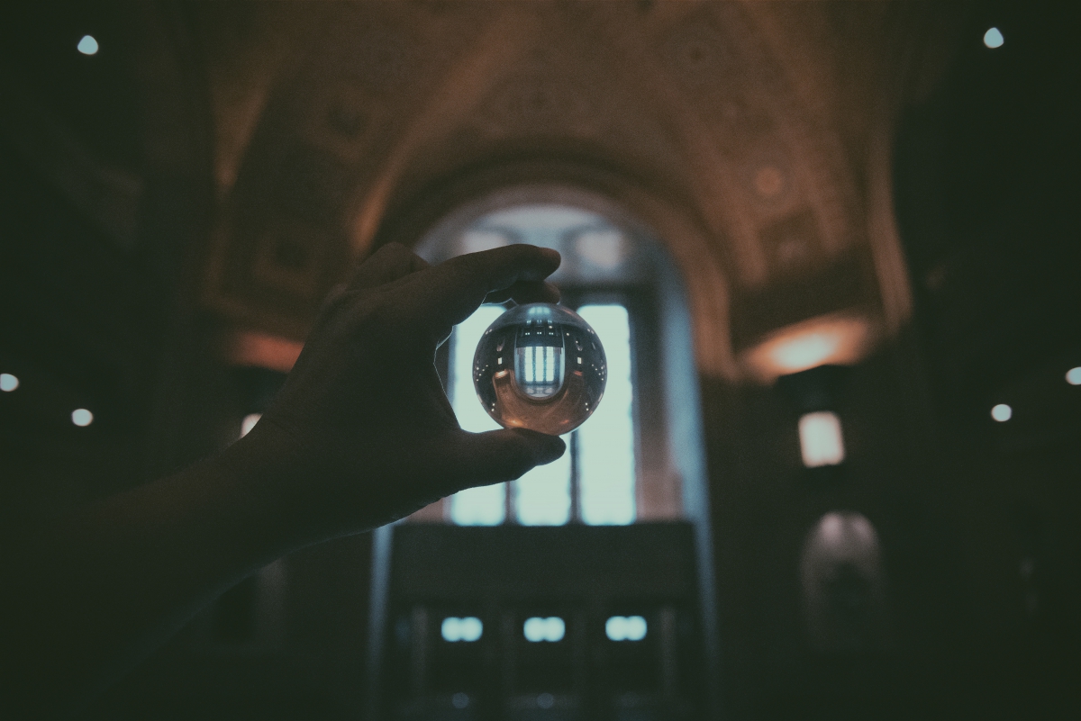 A hand holding a glass sphere in front of a large arched window inside an ornate building.