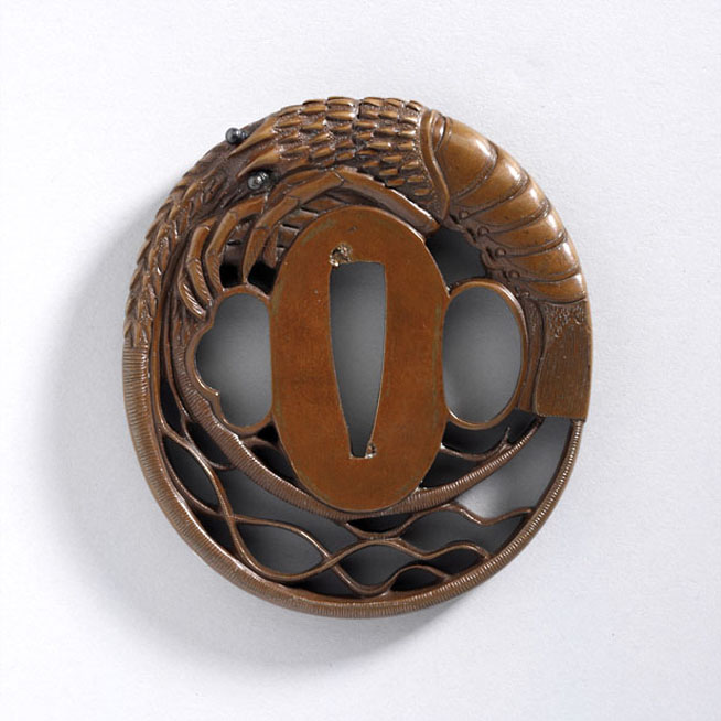 Circular bronze Japanese tsuba with a dragon above stylized waves surrounding the central grip opening.