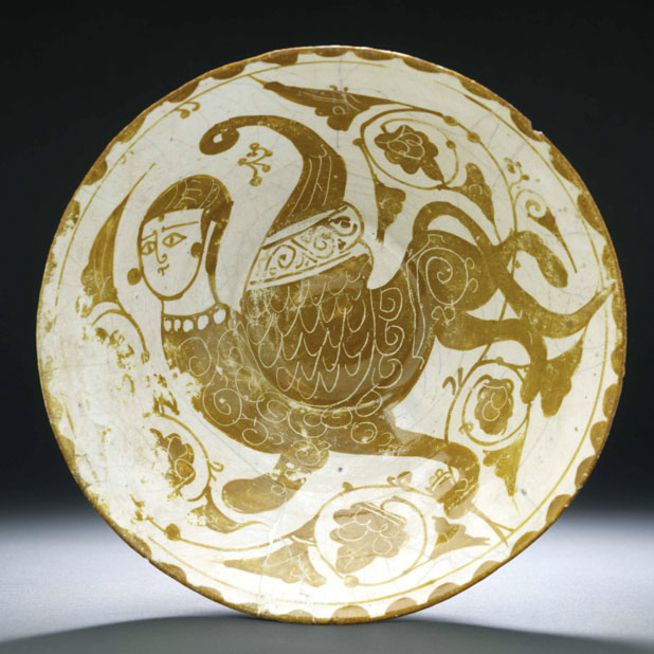 Assiette en céramique ornée d'une créature mythique ailée à tête humaine entourée de motifs tourbillonnants en forme de vigne.