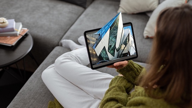 A person holding a tablet displaying an aerial view of a building with surrounding greenery.