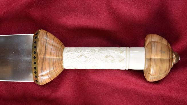Close-up of a dagger hilt with wood and carved bone components against a red fabric background.