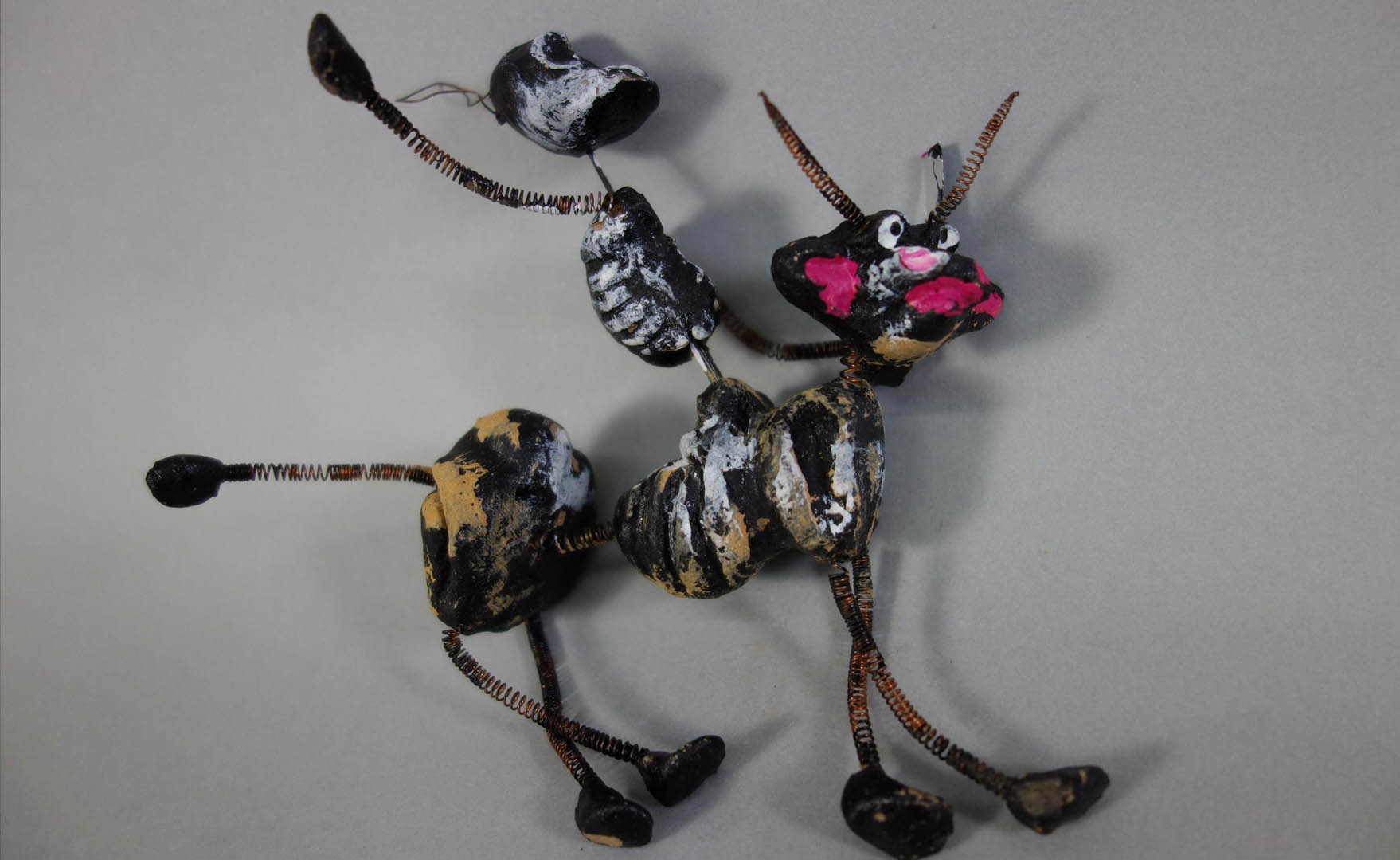 Petit animal en brindilles et bâtons peints sur fond gris.
